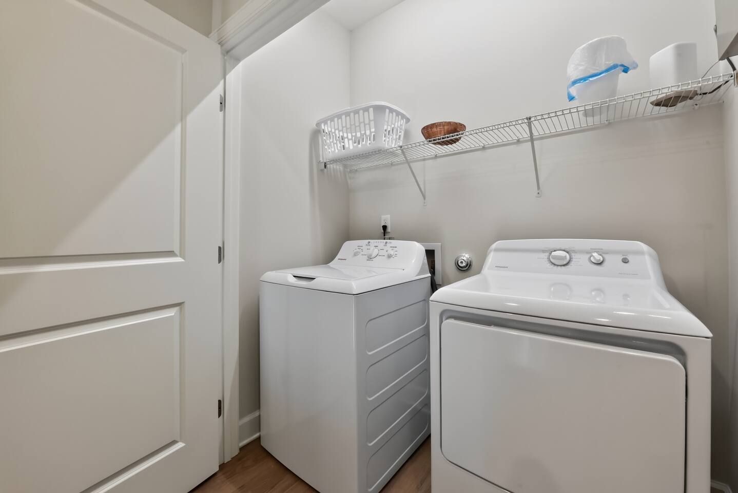 Une buanderie équipée d’un lave-linge et d’un sèche-linge à chargement frontal, d’une étagère en métal avec des paniers et d’une porte blanche.