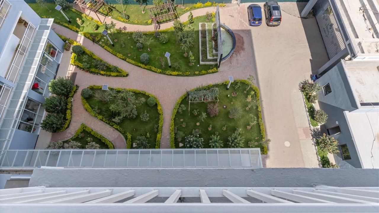 Vista aerea di una zona residenziale con un giardino centrale, un’area giochi e auto parcheggiate.