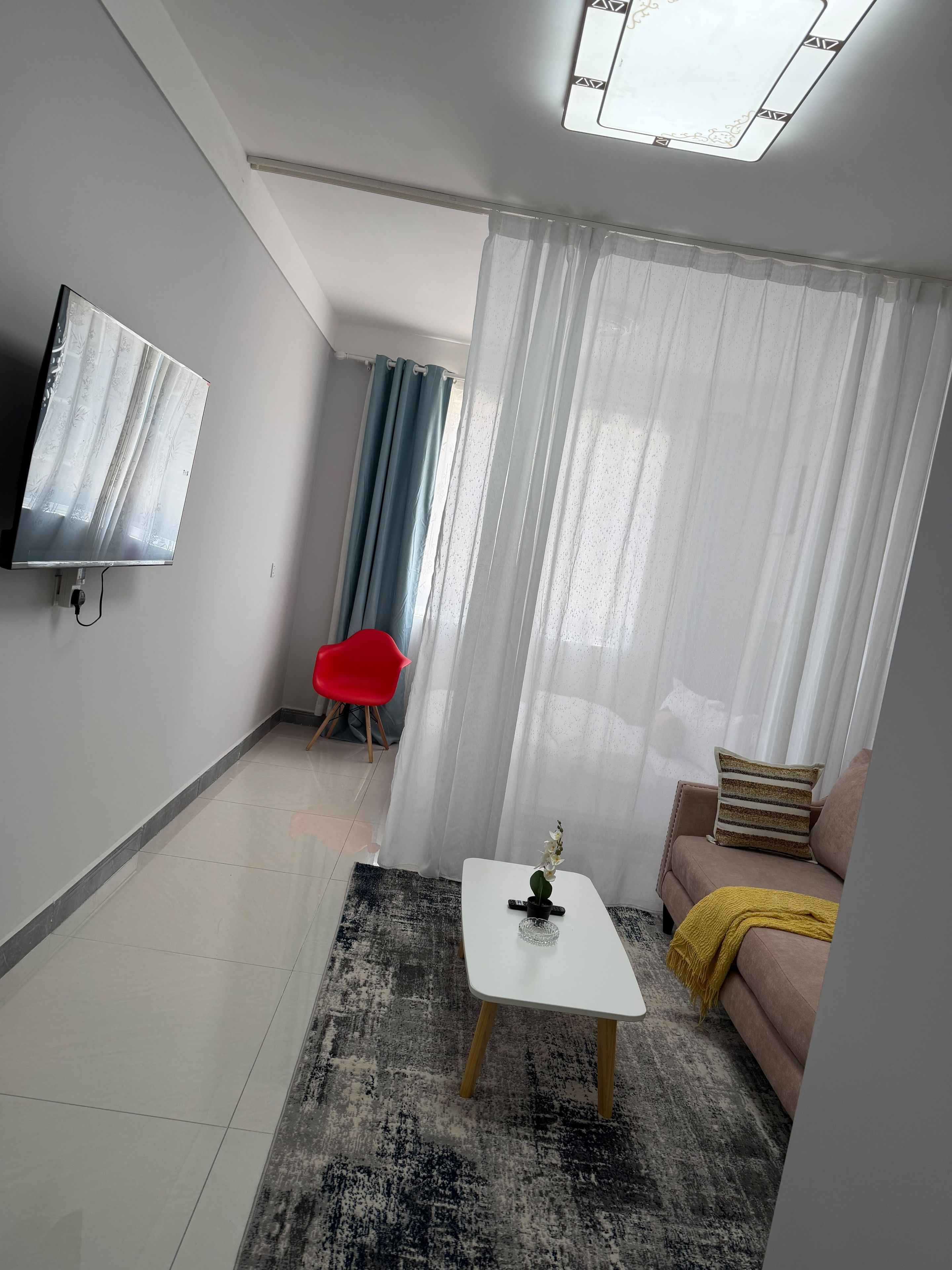 Un soggiorno moderno con una TV a schermo piatto montata a parete, un divano con una coperta gialla, una poltrona rossa e un tavolino da caffè con un oggetto decorativo.