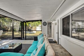 Eine überdachte Terrasse mit einer Couch, einem Couchtisch und einem Dartspiel.