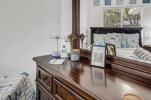 Ein Schlafzimmer mit einem hölzernen Schminktisch, einem Bett mit blau-weißer Blumendecke und einem großen Spiegel, der den Raum reflektiert.