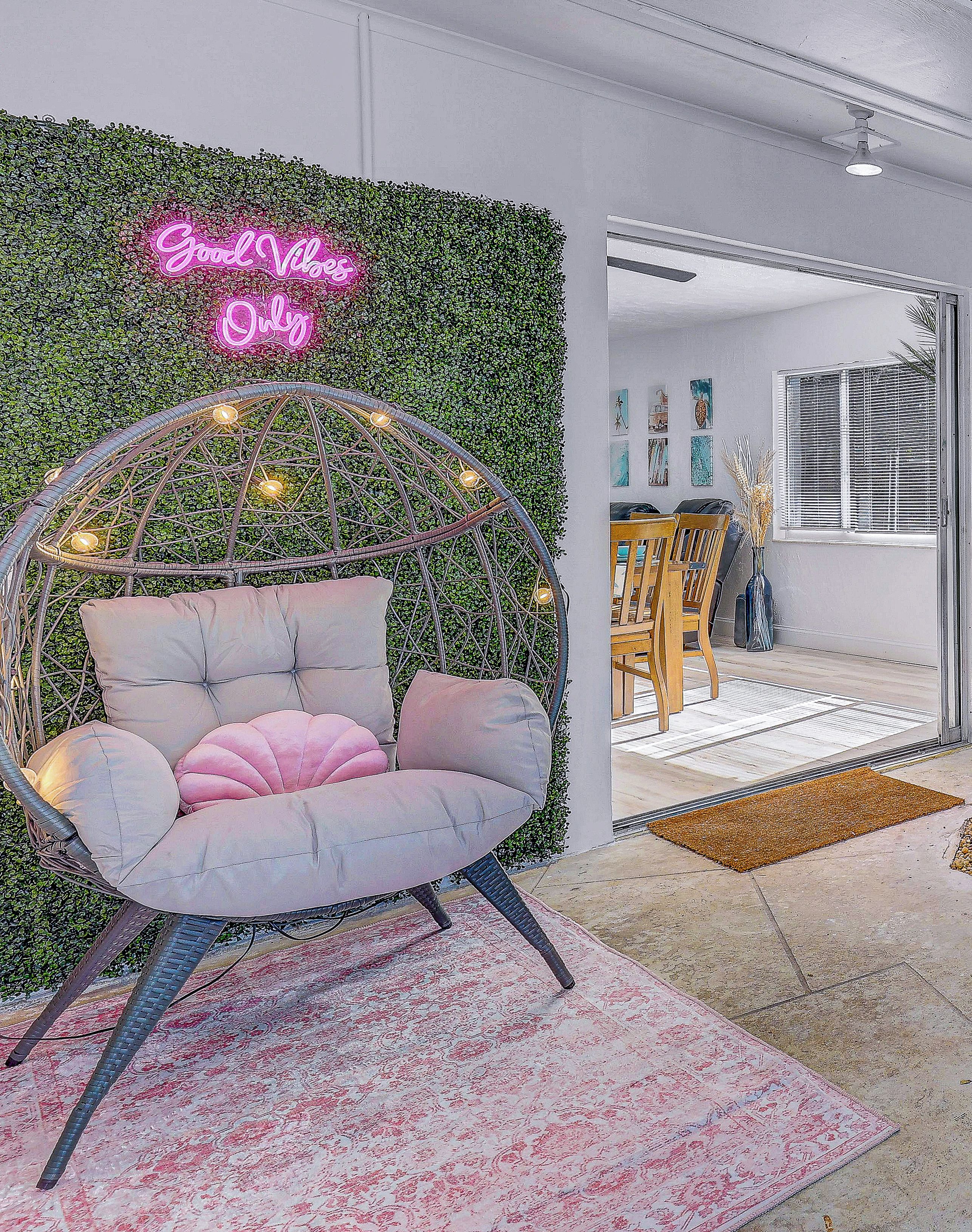 A room with a hanging chair, a green wall with a neon sign, and a dining area with chairs and a table.