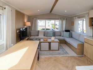A modern living room with a sofa, a TV, a coffee table, and a dining table. - The Beach Retreat at Cayton Bay (Scarborough)