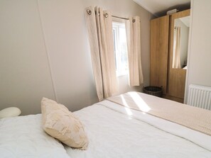 A bedroom with a bed, a window with curtains, a wooden wardrobe, and a radiator. - The Beach Retreat at Cayton Bay (Scarborough)