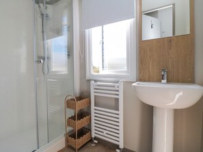 A bathroom with a glass shower enclosure, a white sink, a wooden vanity, and a window providing natural light. - The Beach Retreat at Cayton Bay (Scarborough)