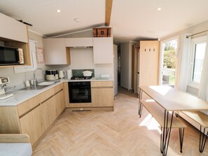 A modern kitchen with a microwave, stove, sink, and wooden cabinets. - The Beach Retreat at Cayton Bay (Scarborough)