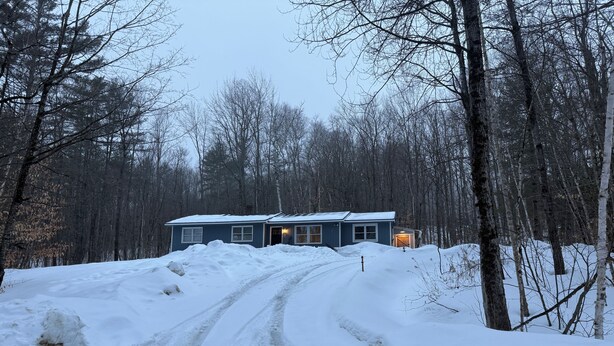 A house with a snow-covered driveway and a forested background. - Secluded 3-bedroom house in Ludlow with cozy Pellet stove (Ludlow)