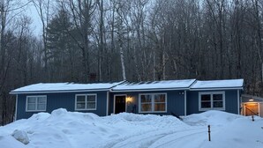 A two-story house with a snow-covered driveway and a forest in the background. - Secluded 3-bedroom house in Ludlow with cozy Pellet stove (Ludlow)