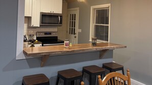 A kitchen with a wooden ceiling, white cabinets, a built-in microwave, and a bar area with stools. - Secluded 3-bedroom house in Ludlow with cozy Pellet stove (Ludlow)