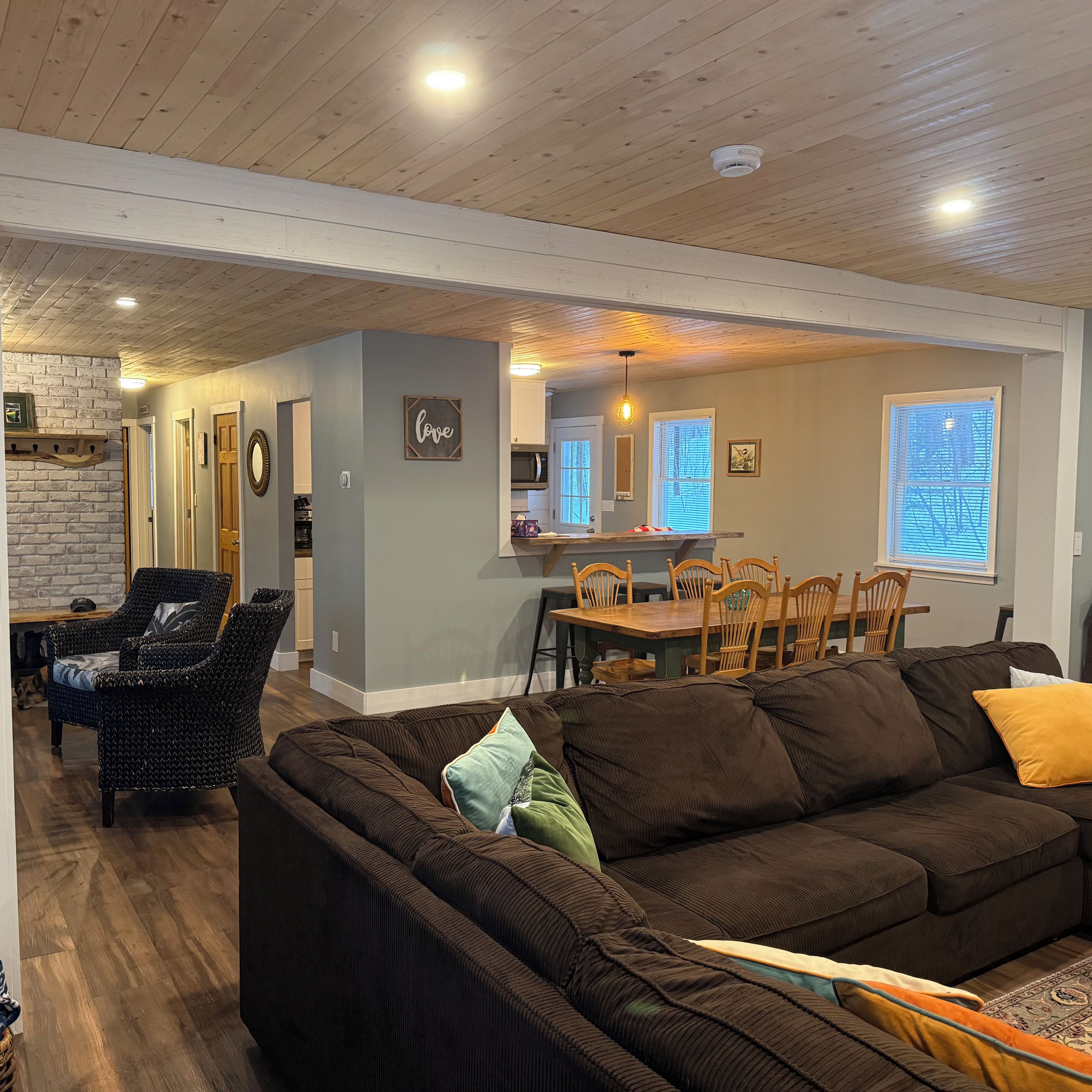 A cozy living room with a dark brown sofa, a wicker chair, and a dining area with wooden chairs and a table.