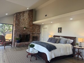 A bedroom with a large bed, a fireplace, a view of the outdoors, and a door to another room. - Spacious 5-bedroom house and Casita with endless views of the Temecula Valley (Temecula)