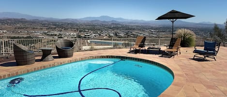 A swimming pool with a view of distant mountains, surrounded by outdoor furniture and a clear sky.