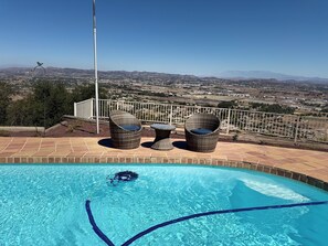A swimming pool with two wicker chairs and a table, surrounded by a tiled deck. - Spacious 5-bedroom house and Casita with endless views of the Temecula Valley (Temecula)