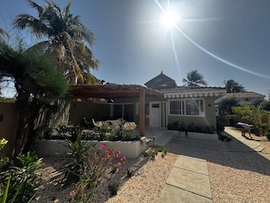 Una casa con un portico coperto, un giardino pieno di piante e un cielo sereno.