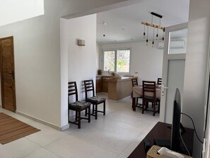 A modern kitchen with a central island, dining area with chairs, and a television on a stand.