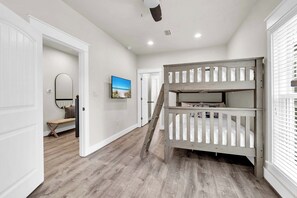 Un couloir avec un lit superposé, un banc, un miroir et un téléviseur fixé au mur.