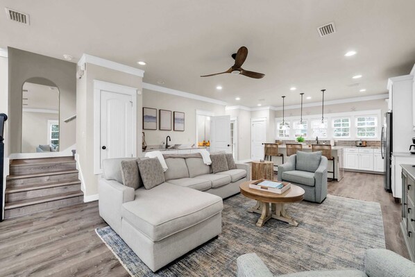 A spacious living room with a sectional sofa, a coffee table, and a dining area with a kitchen in the background. - Come & Sea by Stay on 30a (Inlet Beach)