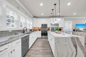 Une cuisine moderne avec des meubles blancs, un îlot en marbre, des appareils électroménagers en acier inoxydable et des luminaires suspendus.