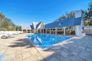 A swimming pool with a covered patio area, lounge chairs, and a building with a sloped roof. - Come & Sea by Stay on 30a (Inlet Beach)