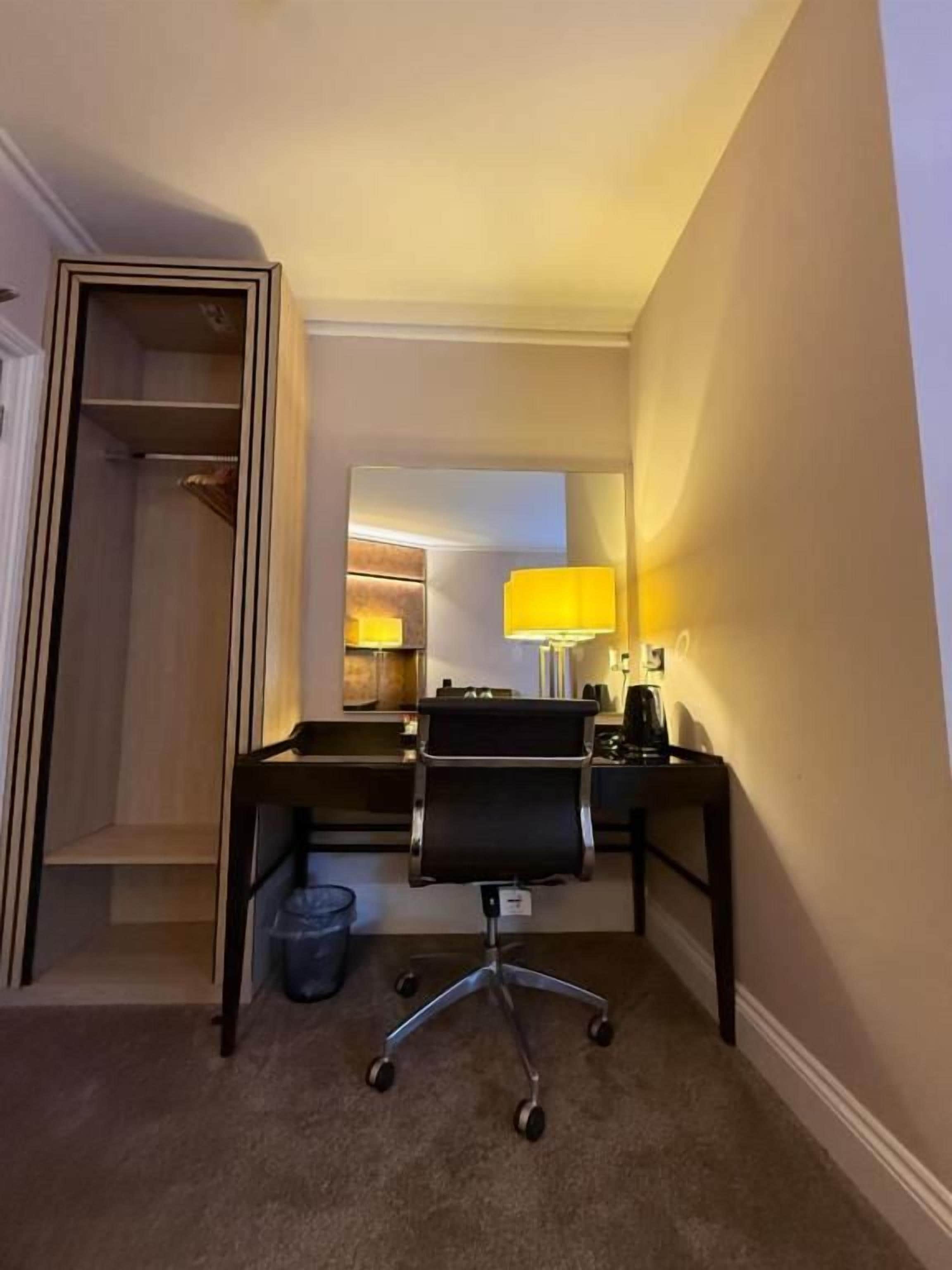 Una habitación de hotel con escritorio, silla y un pequeño cubo de basura.