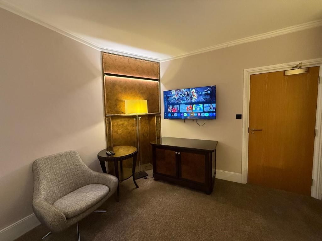 A room with a television mounted on the wall, a small table, a chair, and a door.