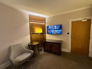 A room with a television mounted on the wall, a small table, a chair, and a door.