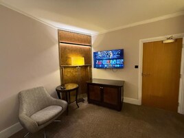 Una habitación con una televisión montada en la pared, una mesita, una silla y una puerta.