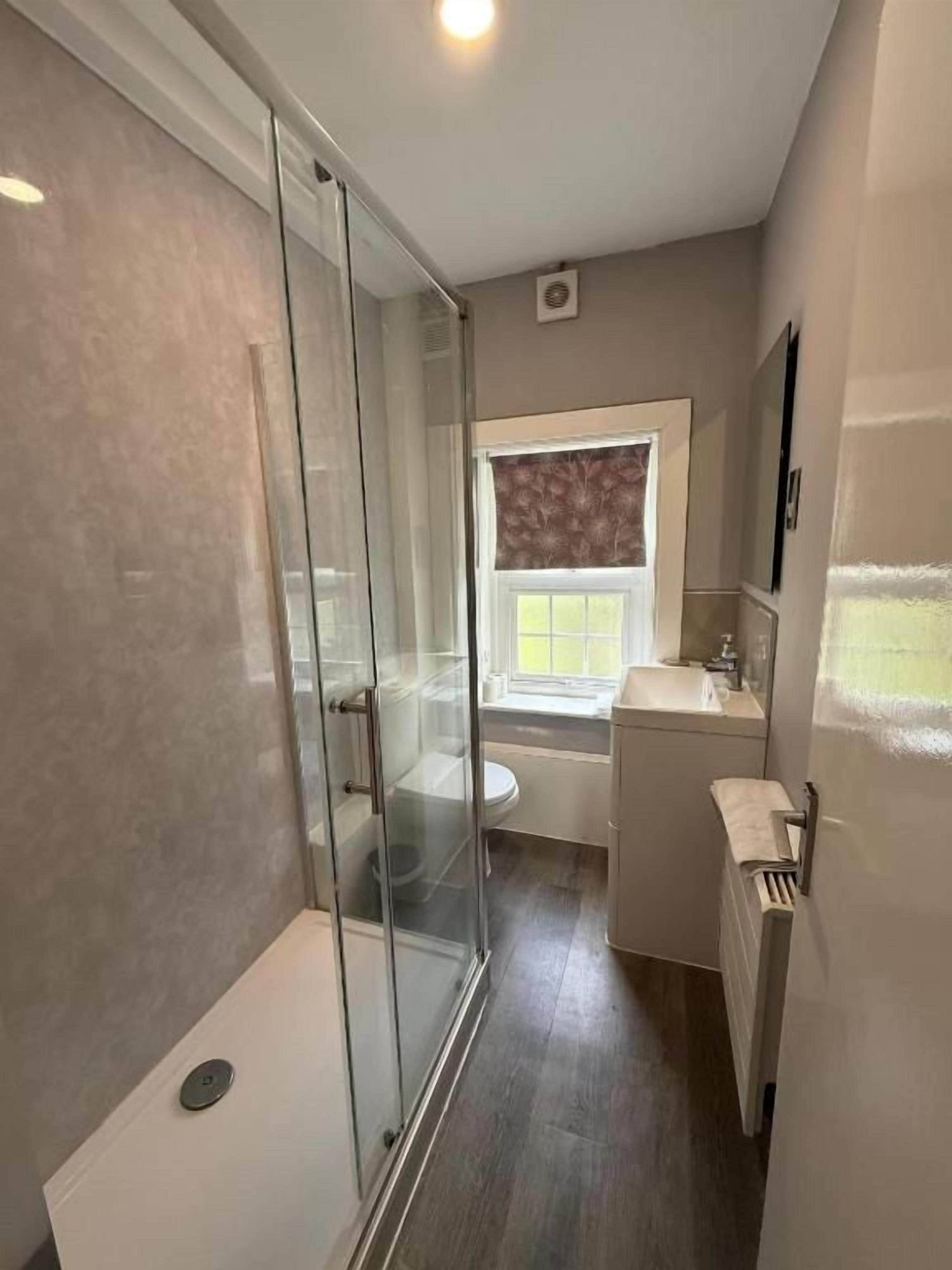 Un baño con cabina de ducha de vidrio, inodoro y lavamanos.