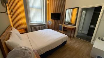 Una habitación de hotel con cama, escritorio, televisión y espejo.
