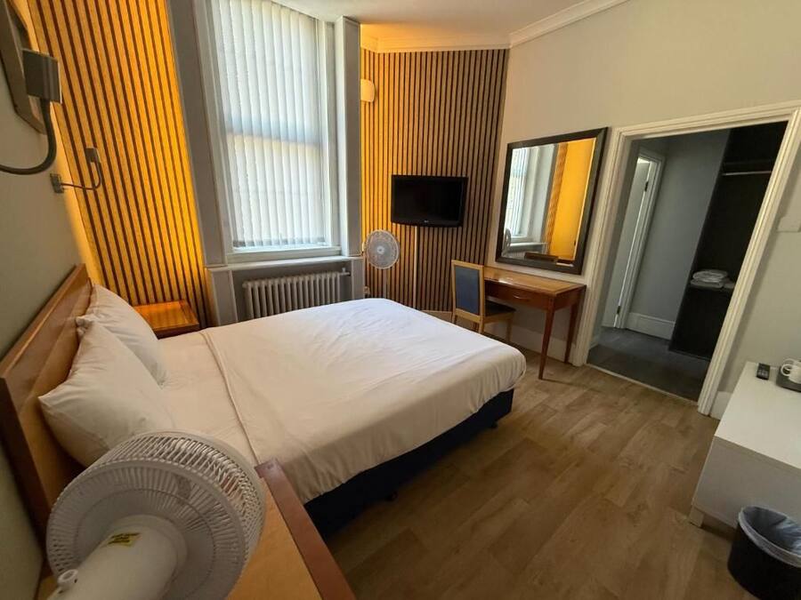 Una habitación de hotel con cama, escritorio, televisión y espejo.