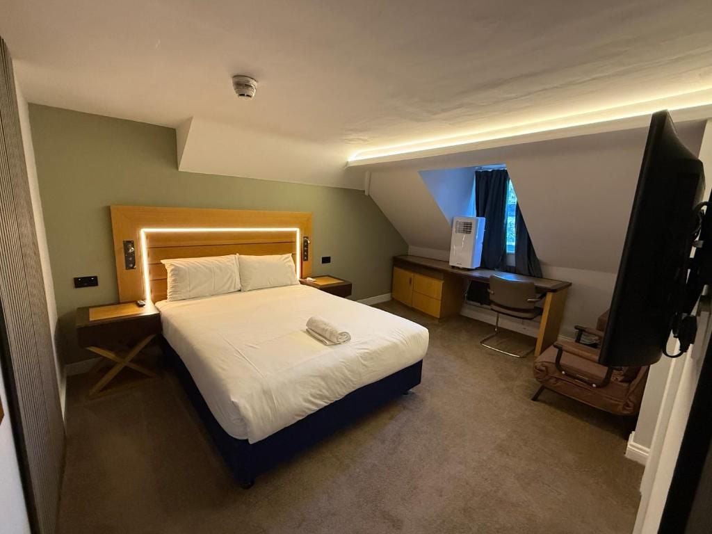 A hotel room with a bed, bedside tables, a desk, and a television.