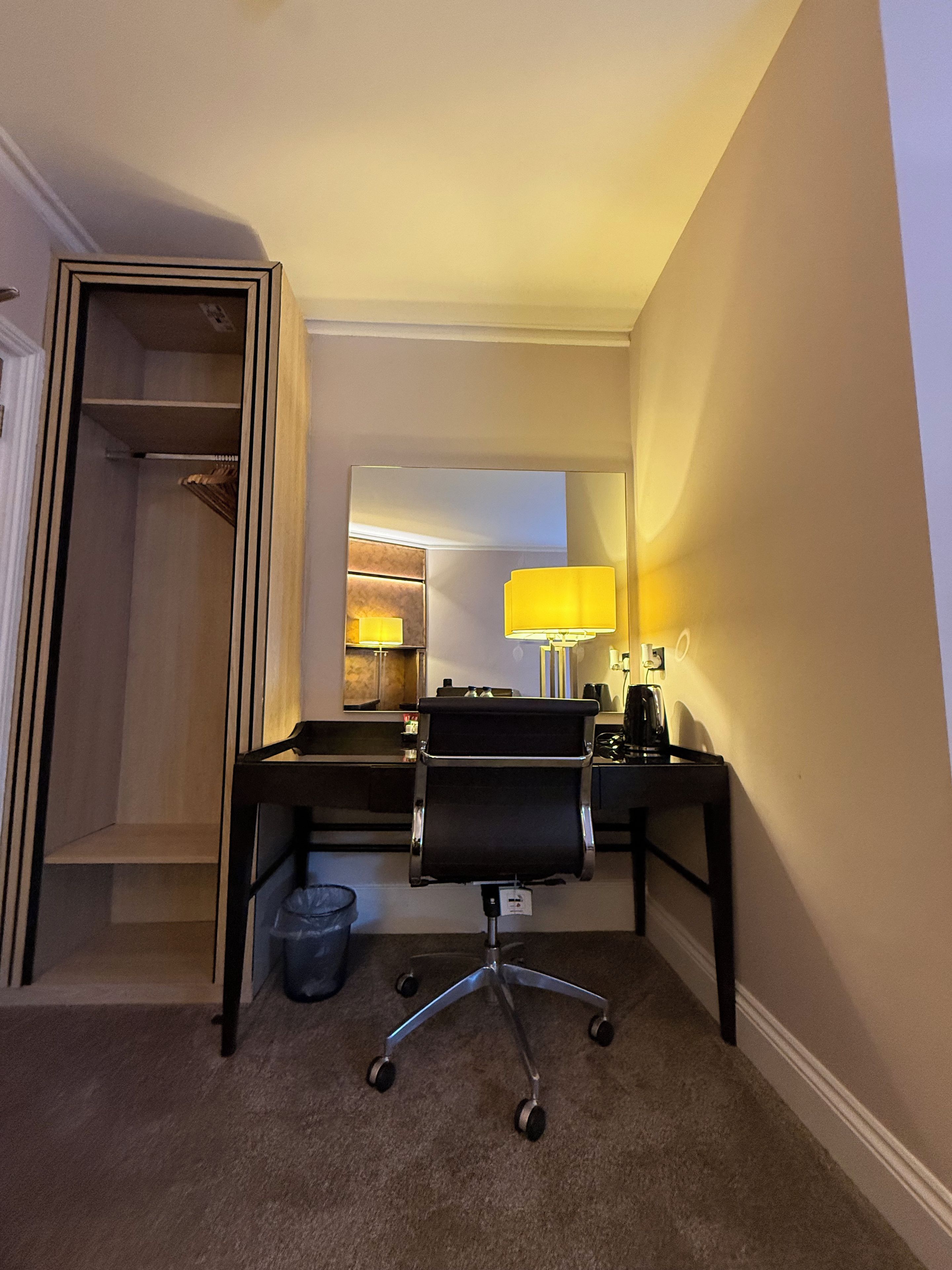 Een hotelkamer met een bureau, stoel, lamp en een spiegel.