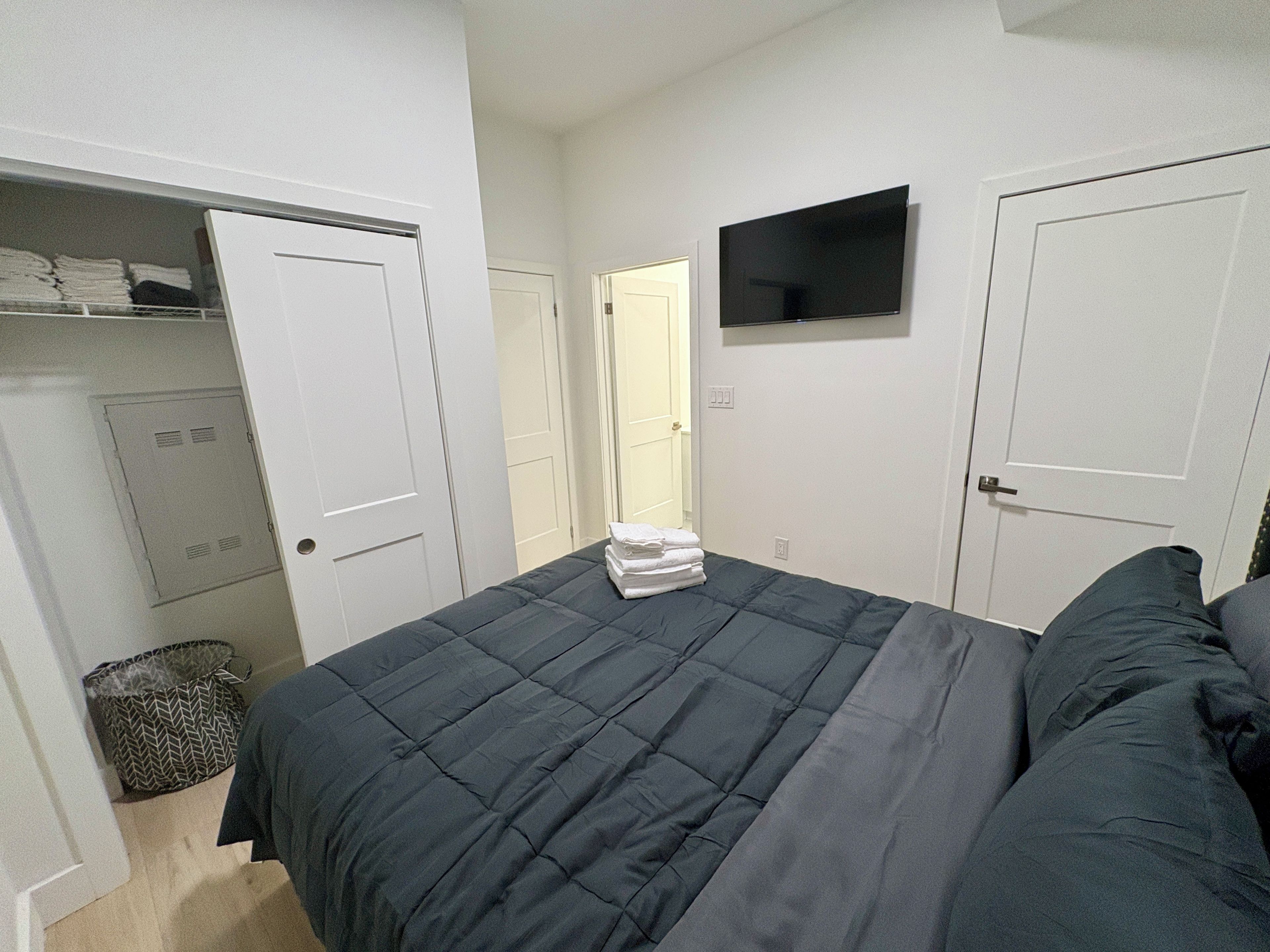 Una camera da letto con un letto, una televisione a parete e un armadio pieno di vestiti ordinati.