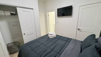 Una camera da letto con un letto, una televisione a parete e un armadio pieno di vestiti ordinati.