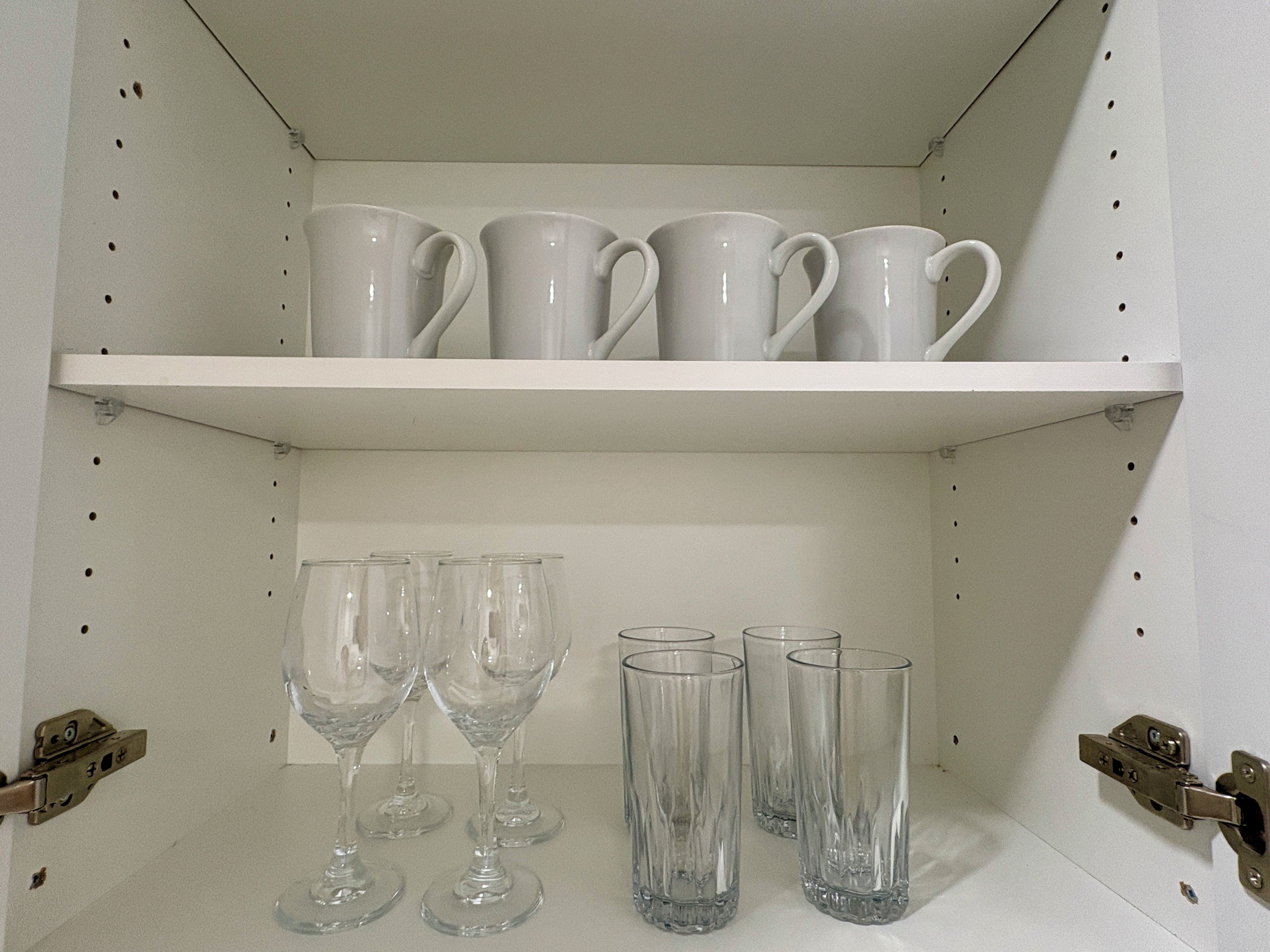 Una estantería con tazas blancas y vasos de vidrio.