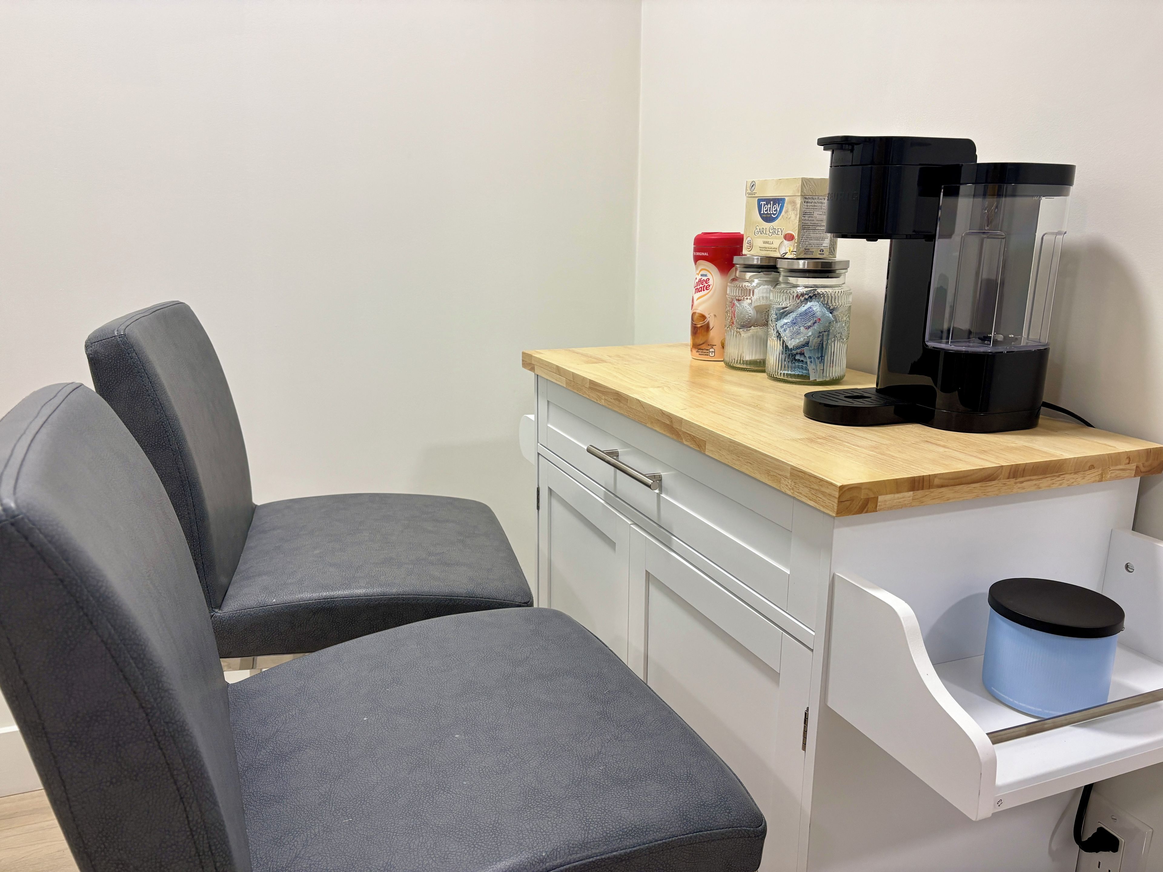 A kitchenette with a coffee maker, jars, and a red container on the counter.