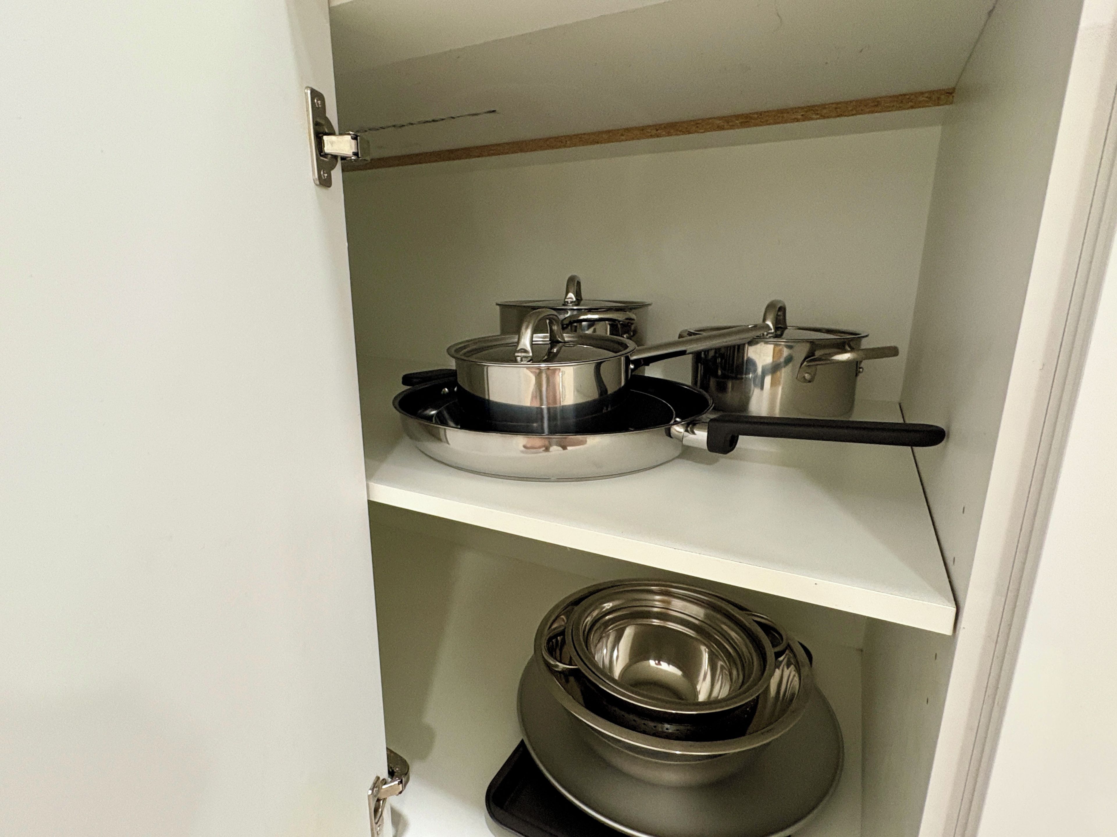 A kitchen with stainless steel cookware on a white shelf.