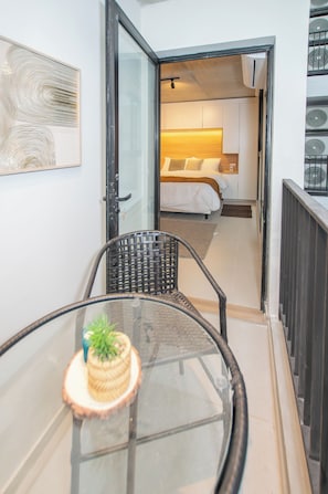 Una habitación con una cama, una pequeña mesa con una planta y una puerta que da a otra estancia.