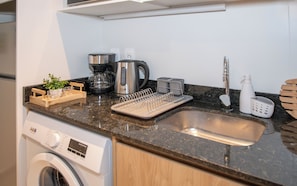 Una cocina equipada con lavadora, cafetera, hervidor y un lavamanos con grifo.
