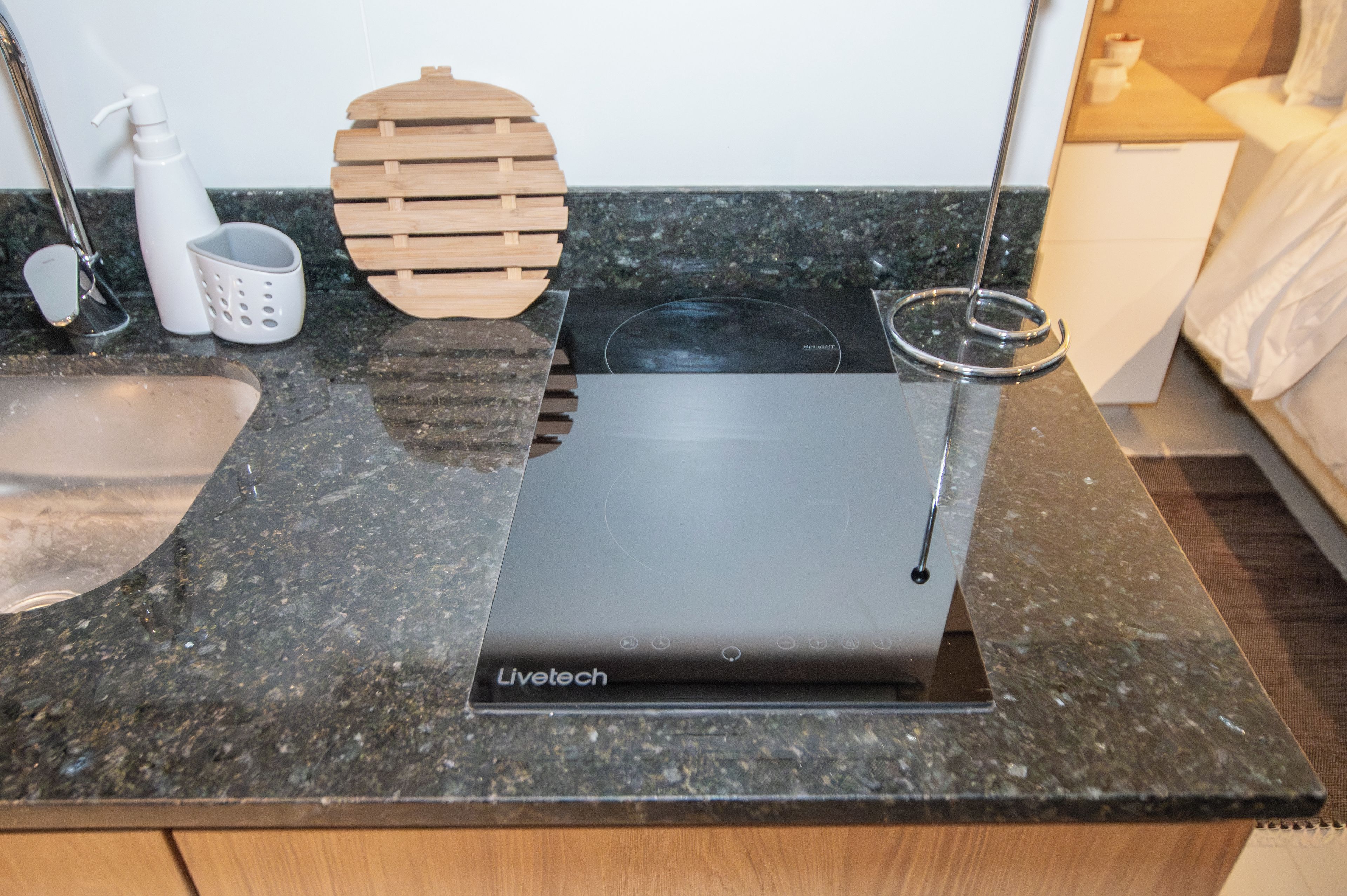 A kitchen with a countertop, a sink, a wooden cutting board, a white soap dispenser, and a black appliance labeled 'Livetech'.
