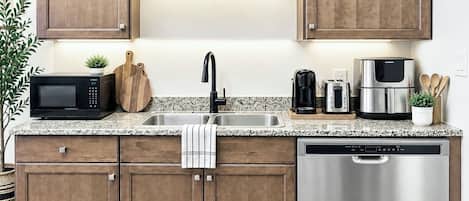A kitchen with wooden cabinets, a stainless steel dishwasher, a microwave, a coffee maker, and a toaster.
