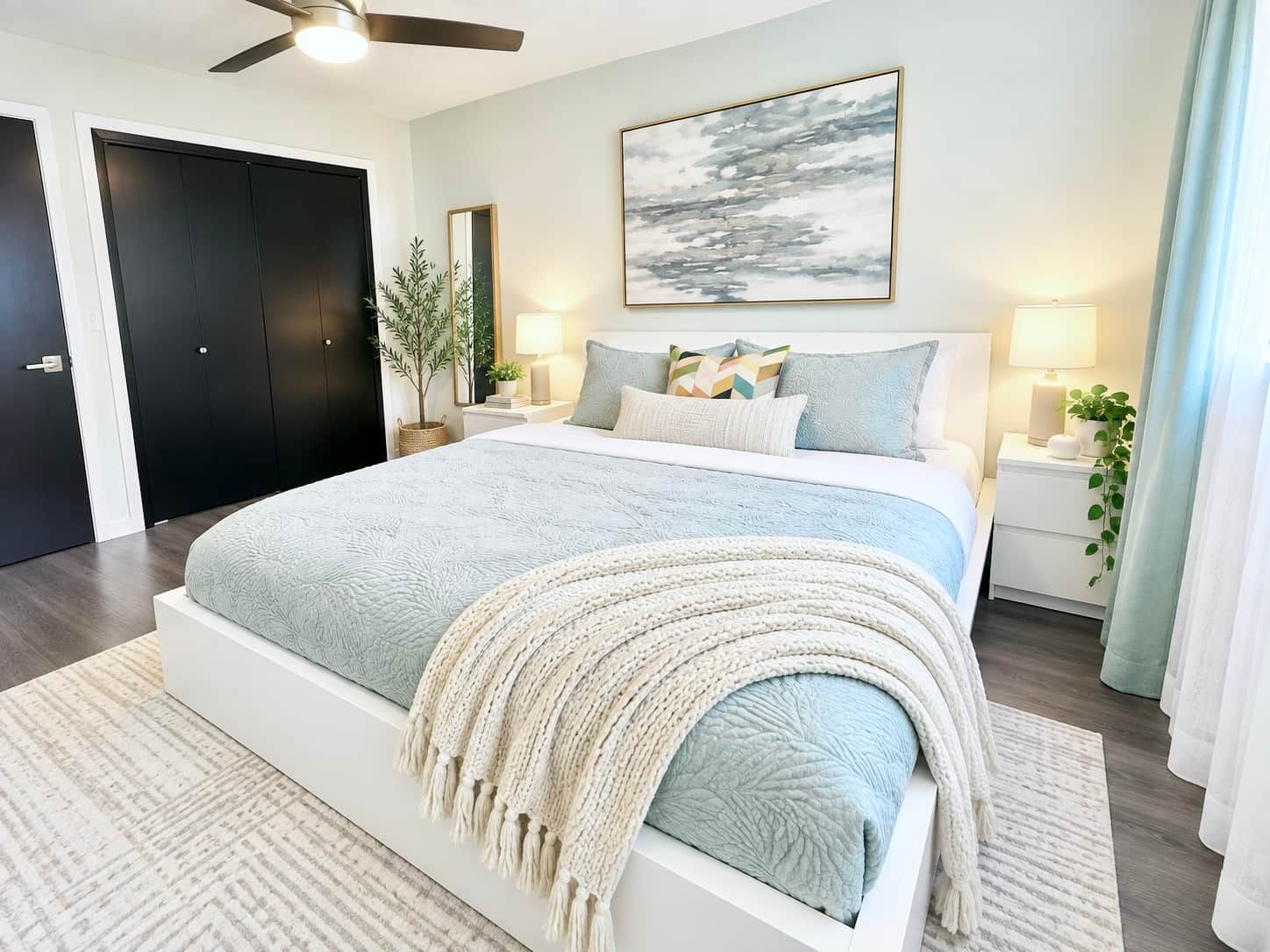 Quarto com cama grande, mesas de cabeceira, ventilador de teto e uma obra de arte na parede.
