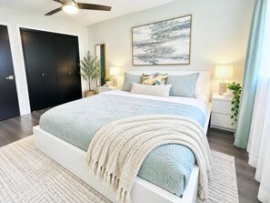 Ein Schlafzimmer mit einem großen Bett, Nachttischen, einem Deckenventilator und einem an der Wand befestigten Kunstwerk.