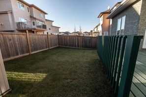 A residential backyard with a wooden fence, a grassy lawn, and a building with a balcony. - CozyHouse*5BR*FamilyBaby&KidFriendly*KingBed*A/C* (Edmonton)