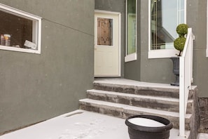 Un escalier menant à une porte, une fenêtre avec vue et un jardinier avec un petit arbre.