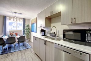 Een moderne keuken met een eethoek, met daarin een magnetron, spoelbak en kastjes.