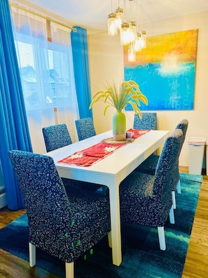 A dining area with a white table, blue patterned chairs, a vase with yellow flowers, and a colorful abstract painting on the wall. - Family Baby&Kid Friendly*Close toUofA*Kingbed*3BR* (Edmonton)