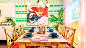 Un coin repas avec une table en bois dressée pour six personnes, entourée de chaises. Un tableau abstrait aux couleurs vives est accroché au mur, au-dessus de la table.