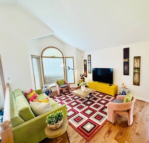 A modern living room with a green sofa, a yellow cabinet, a large TV, and a patterned rug. - KidsParadise*Kingbed*NearWEM*BabyFamilyKid Frienly (Edmonton)