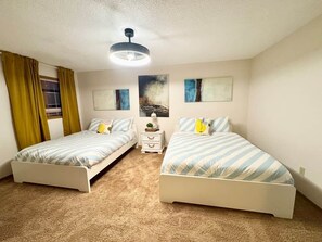 A bedroom with two single beds, a ceiling fan, a nightstand with a lamp, and artwork on the walls. - KidsParadise*Kingbed*NearWEM*BabyFamilyKid Frienly (Edmonton)